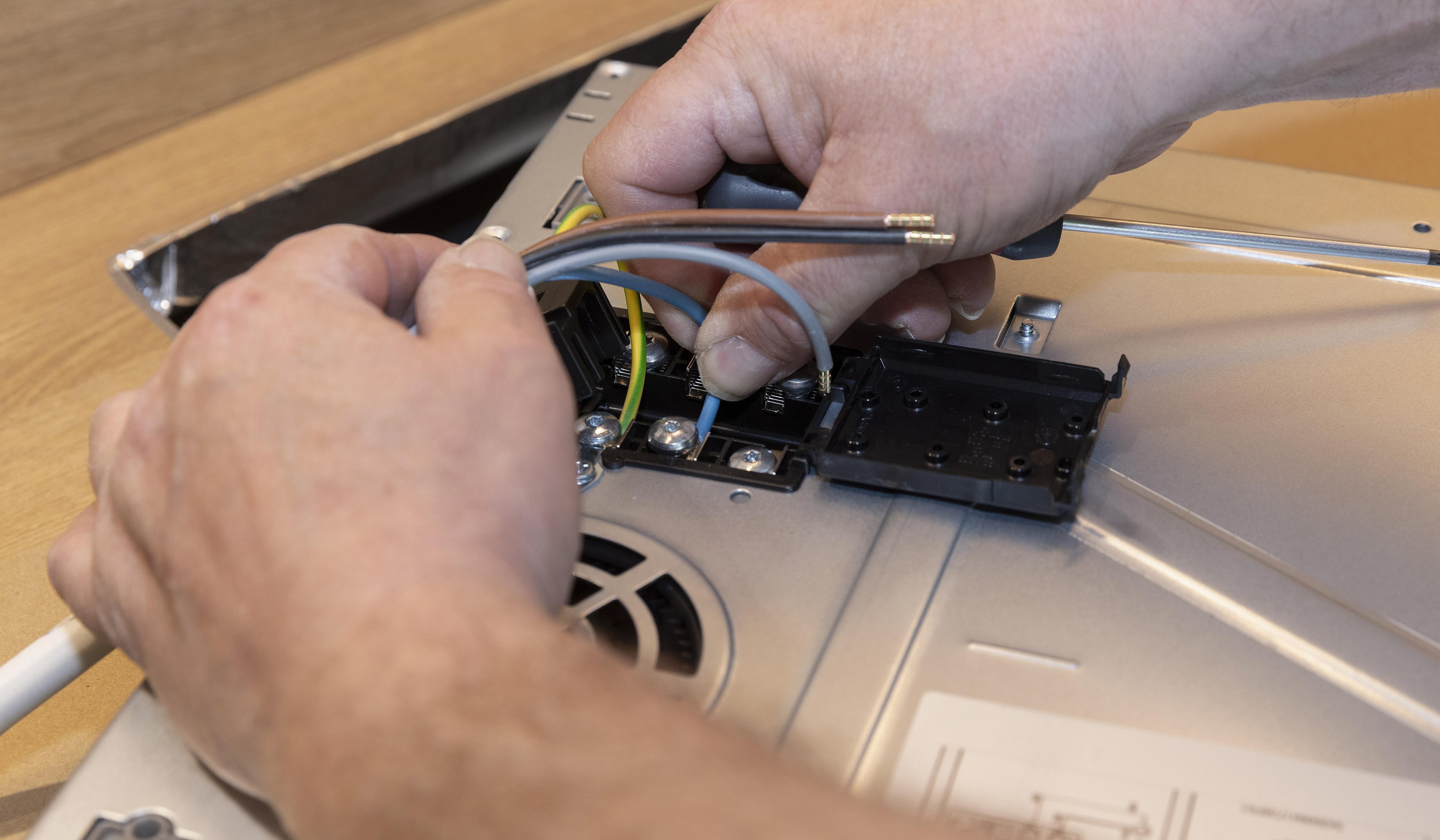 Hände schließen Kabel an ein elektrisches Gerät an.