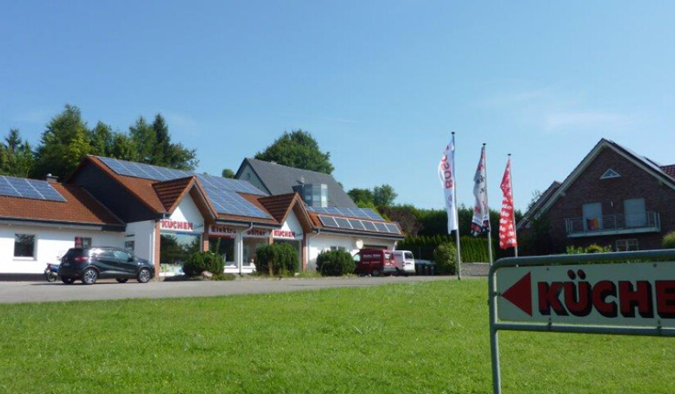 Gebäude mit Solaranlagen, Fahnen und Küchenschild an sonnigem Tag.